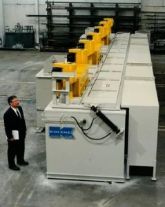 Long white process line with yellow hoist frames beside a man in a suit, with a Kolene logo on the tank