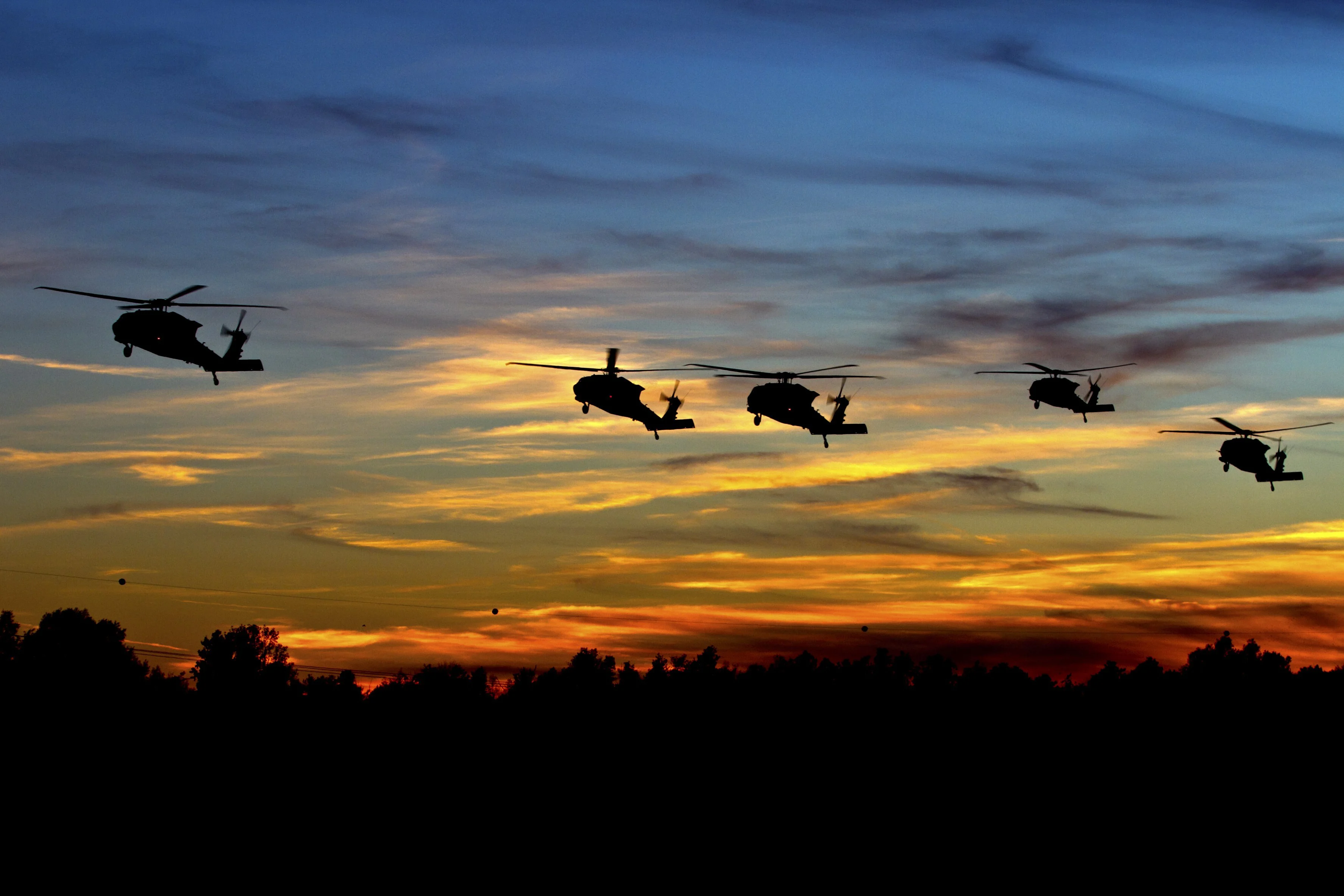 Five UH-60 Black Hawk helicopters silhouetted against a gold and blue sunset.