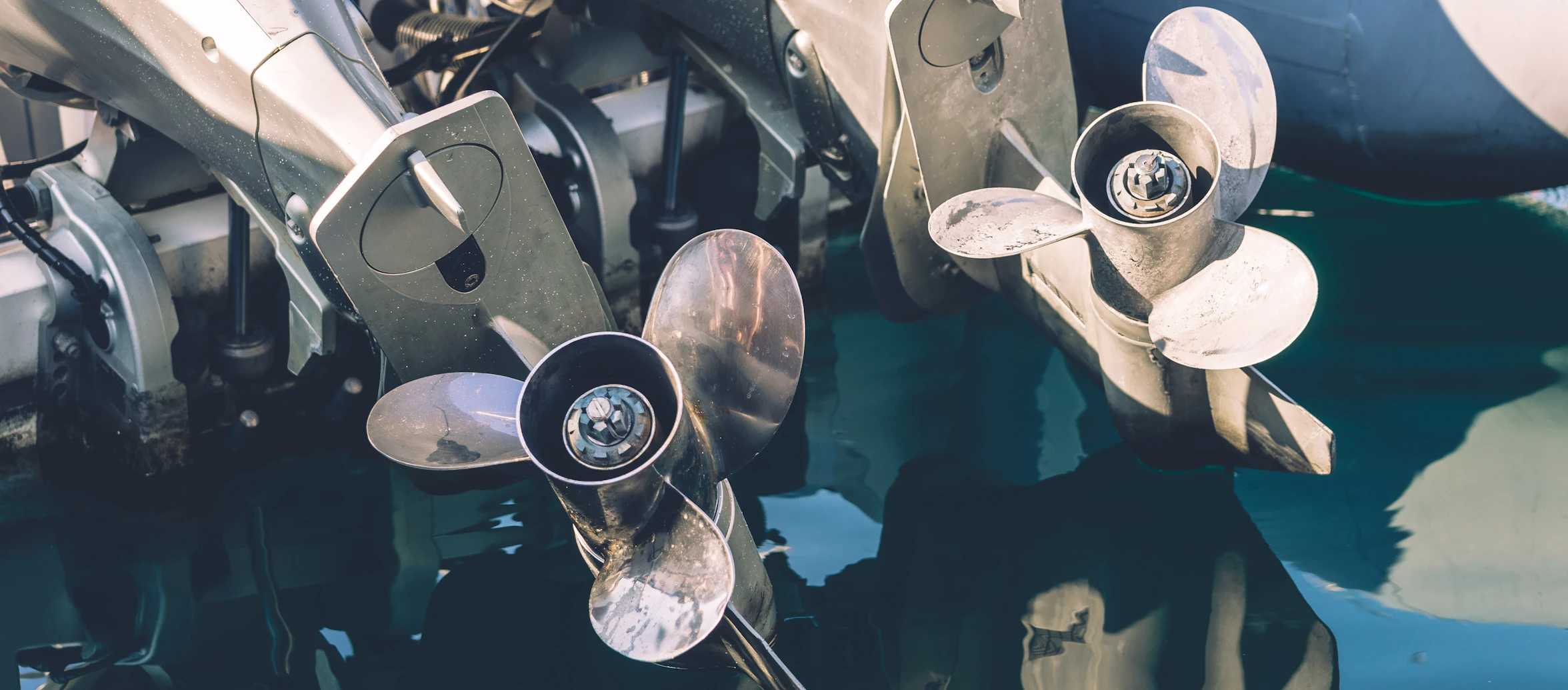 Stainless steel propellers on the lower units of two outboard motors, tilted up above the water