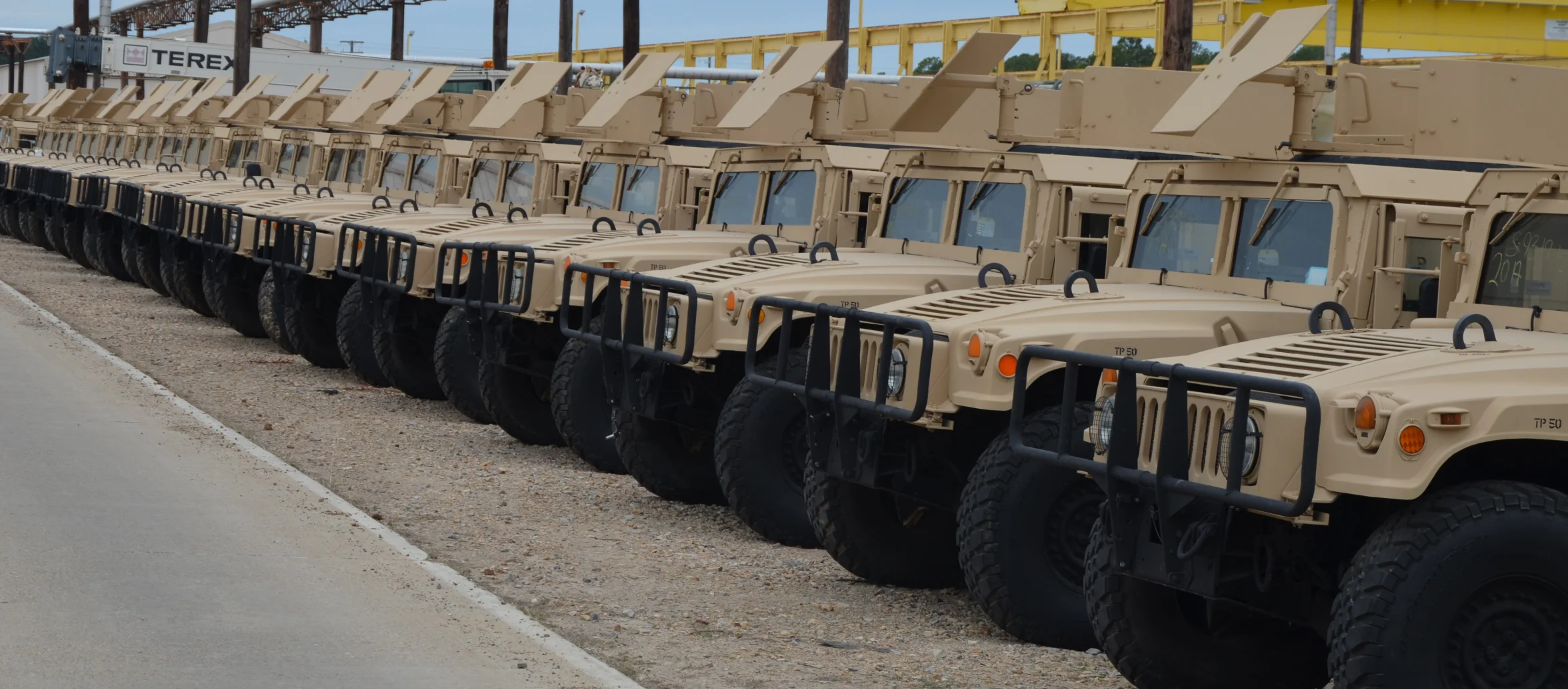 A long row of tan, up-armored Humvees parked side by side at Red River Army Depot in Texas
